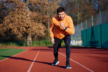 Man in orange sports jacket starting sprint on outdoor running track in stadium