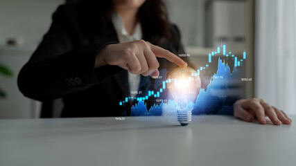 A businesswoman touches a glowing light bulb as financial graphs and data surround her, symbolizing the intersection of creativity and analytics in today economy. Scalp