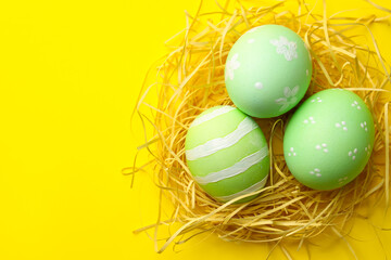 Many painted Easter eggs and straw on yellow background, top view. Space for text