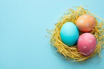 Many painted Easter eggs and straw on light blue background, top view. Space for text