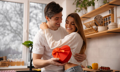 Romantic couple holding red heart shaped gift together looking into eyes