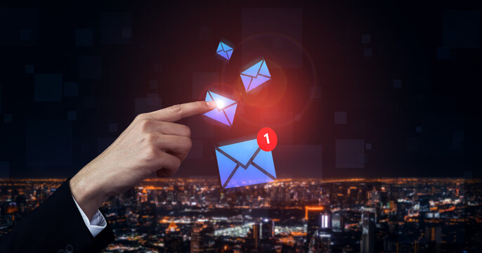 A hand reaches towards floating email icons illuminated against a vibrant night cityscape, symbolizing communication, digital connectivity, and modern technology. Gantry - Powered by Adobe