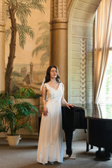 The bride elegantly stands beside a grand piano in a stunning historic venue, where a beautiful...