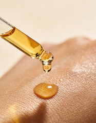 golden oil is pouring out of a glass dropper on dark skin, macro texture of the skin on which the oil is applied