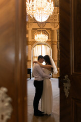 Fototapeta premium Couple embraces in a grand hall during their wedding ceremony at a historic venue with chandeliers and elegant decor