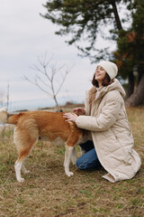 Fototapeta premium Woman kneeling in a beige coat and beanie outdoors, patting a friendly dog in an autumn field, calm moment of companionship and nature, soft light and gentle breeze, park scenery