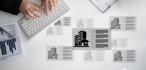 A person types on a computer keyboard, surrounded by displayed real estate listings and graphs,...