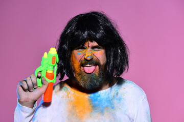 Funny crazy man with beard and wig in holi color on face. Expressive crazy male portrait with paint on face. Crazy male emotions and fun. Crazy funny bearded man in wig.