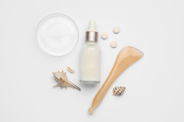 Bottle of cosmetic serum with pills and massage tool on white background