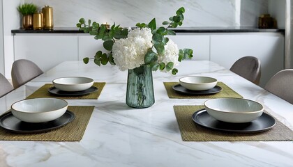 modern dining table with a white marble top on the table there is a vase with white flowers and greenery in it next to the vase there are two small bowls and a small bowl