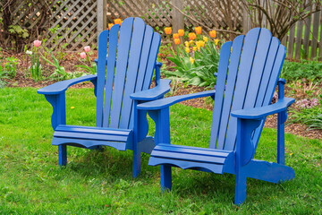 A pair of blue Adirondack chairs in a backyard garden.