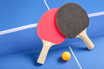 Different ping pong rackets and ball near net on blue table