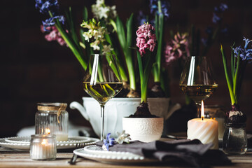 Spring elegant wedding or Easter celebration table decor. Festive white china, floral decoration with blooming bulbous hyacinth. Dark background. Springtime home gardening