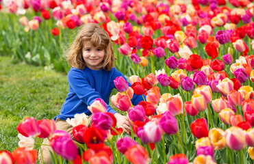 Fototapeta premium Spring dreamy vibe. Kid by blooming tulips. Cute kid portrait in spring garden. Child rest in sunny springs. Spring face child. Dreamy kid in spring garden.