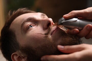 Barber trimming man's mustache in barbershop, closeup