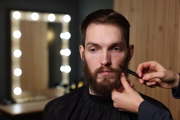 Barber combing man's beard in barbershop, closeup. Space for text