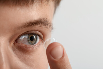 Man putting on contact lenses against light background, closeup. Space for text
