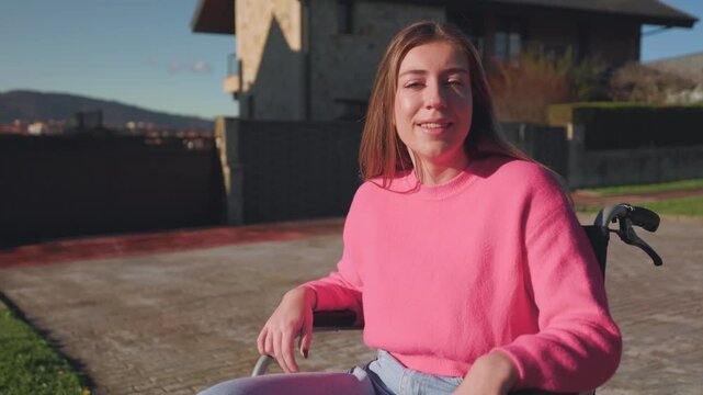 Positive young paraplegic woman sitting in a wheelchair and looking at the camera with a confident smile, enjoying a sunny day outdoors in a residential area of the city