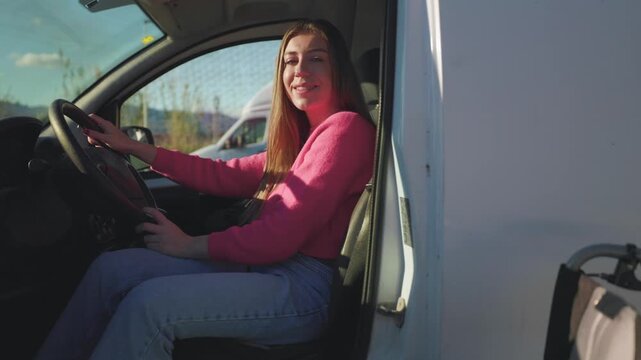 Young paraplegic woman with a disability smiling at the camera while sitting in the driver's seat of her specially adapted vehicle, with her folded wheelchair visible outside the open door