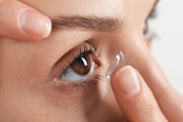 Woman putting on contact lenses against light background, closeup
