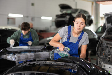 Woman auto mechanic using a grinding machine prepares car parts for painting