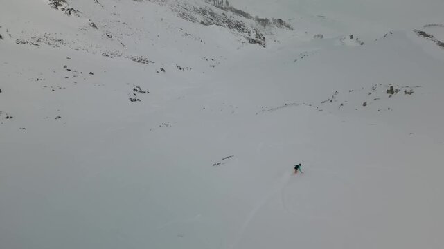 A snowboarder moves through deep powder on a remote mountain slope in Gulmarg, Kashmir. The untouched snow, vast alpine scenery, and dynamic ski tracks highlight the excitement of freeriding