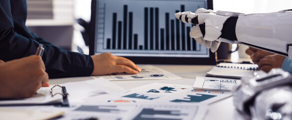 A human and robotic hand interact in a collaborative business environment, analyzing data charts on screens while enhancing decision-making in modern workplaces.Noogenesis