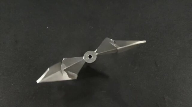 Geometric Metal Object on a Dark Surface: A sleek, modern metal object with sharp angles and a central hole rests gracefully against a dark backdrop, perfect for an industrial or artistic design.