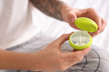Young man with pillbox sitting on bed in bedroom, closeup