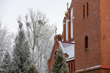 Red brick Orthodox church with golden dome and crosses in snowy winter landscape.
