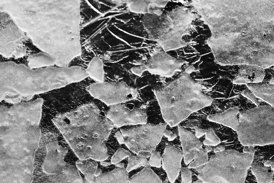 Cracked natural ice surface with frozen patterns and fractures, abstract winter texture background symbolizing cold, climate and fragile nature.