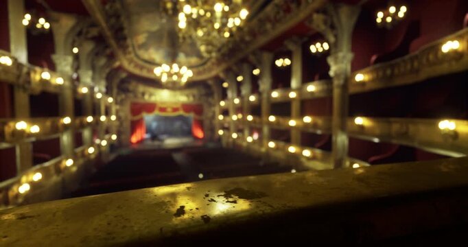 The theater features magnificent chandeliers illuminating the elegant decor. Rows of plush seats are visible, hinting at a performance about to begin. Warm lighting creates a cozy atmosphere.