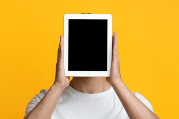 Gadgets addicition, virtual life cocnept. Closeup of man holding pad over his head, unrecognizable guy hiding behind digital tablet with empty screen, mockup, yellow studio background