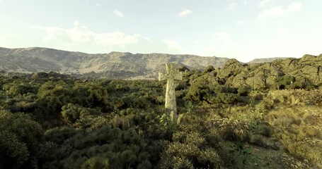 A moss covered cross stands tall in a sprawling landscape of hills and lush foliage. The warm glow of sunset casts a serene atmosphere over the natural setting.