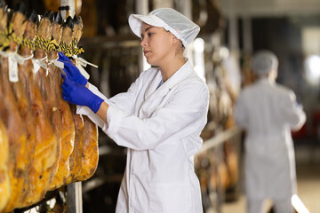 Employee of the jamon factory in a protective uniform keeps the product in a refrigerated room....