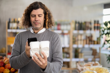 Checking expiration date of yogurt - male shopper scans QR code on label of yogurt using her...