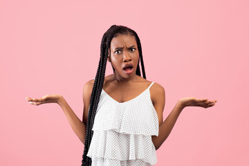 Irritated African American woman showing I DON'T KNOW gesture, shrugging shoulders on pink studio...