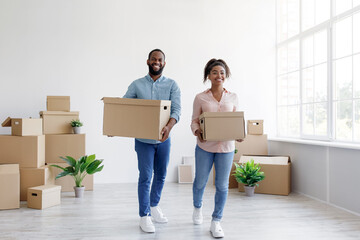 Cheerful millennial african american couple carry cardboard boxes with things in room interior....