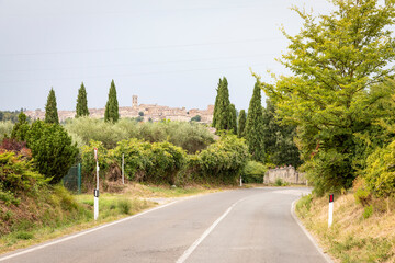 Naklejka premium Paved road on a green landscape with a view to Colle di Val d'Elsa, province of Siena, Tuscany, Italy