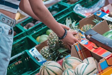 A young woman buys fruit at the supermarket and takes fresh fruit out of a box with her hand.