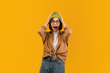 Shocked woman raising hands up and touching head over yellow studio background, emotional caucasian...