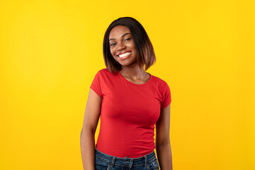 African American Lady Posing Smiling To Camera Standing Over Yellow Studio Background, Wearing Red...