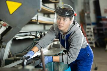 During production of glass products, woman employee wearing clear protective face shield controls production process and is in area of operating equipment.