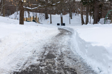 Winter road in the park with salt and melting snow. Pathway in residential neighborhood.