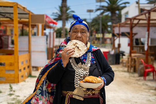 Indigenous mapuche woman in traditional dress and jewelry eating alip&iacute;n bread