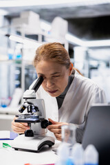 Quality control inspector in lab checking product surface for tiny defects using microscope. Factory worker ensuring manufacturing standards by examining small parts closely with optical device