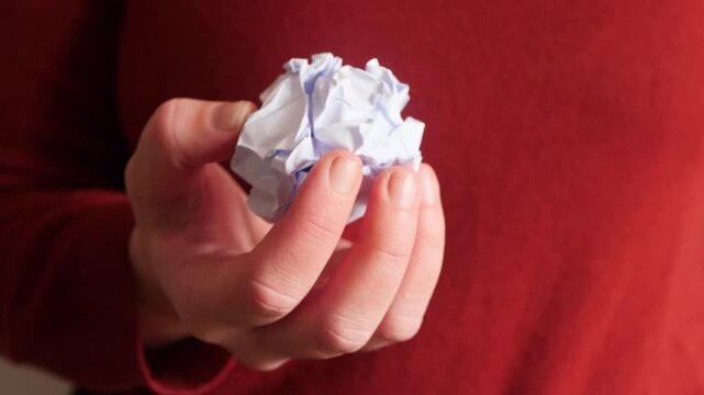 Close up of hand holding crumpled white paper ball. symbolizes frustration, rejection and creative struggle, expressing emotional tension and decision making