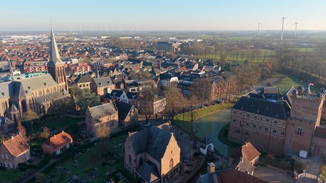 Aerial view of Dutch town with castle, moat, church spire, gabled rooftops, flat fields, and wind turbines blending tradition and innovation.