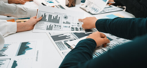 A group of business professionals engaged in an insightful discussion at a table, analyzing various charts and data reports to enhance project strategies and growth. SACTR