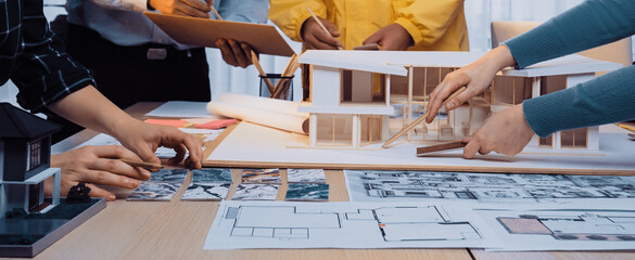 A diverse team of professionals engages in an architectural design meeting, reviewing blueprints and 3D models in a bright, modern workspace. SACTR